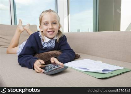 Portrait of little girl holding calculator while lying on sofa