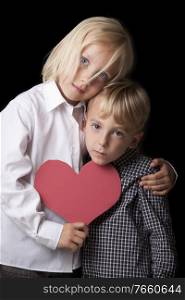 Portrait of little girl holding heart shaped paper with younger brother