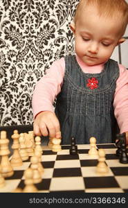Portrait of little girl in denim dress playing chess. Vertical format. Indoor.