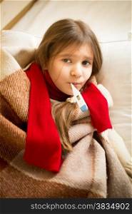 Portrait of little girl lying in bed and holding thermometer in mouth