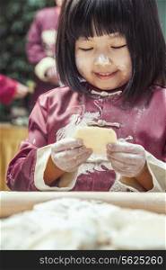 Portrait of little girl making dumplings in traditional clothing