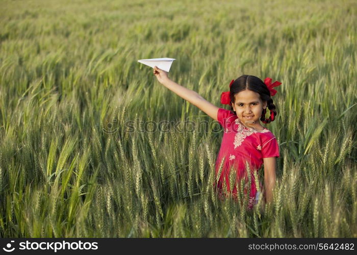 Portrait of little girl playing with a paper aero plane in wheat field