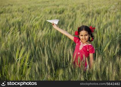 Portrait of little girl playing with a paper aero plane in wheat field