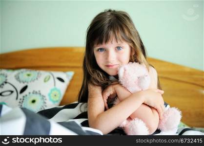 Portrait of little girl sitting in bed with a toy in early morning