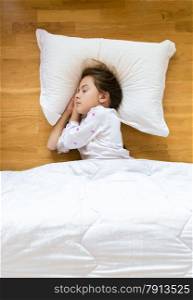 Portrait of little girl sleeping on wooden floor on white pillow