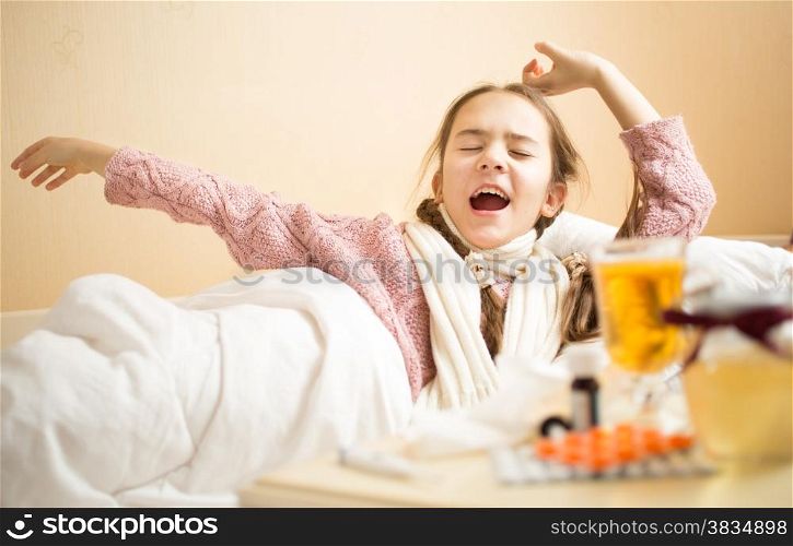 Portrait of little girl with flu yawning in bed at morning