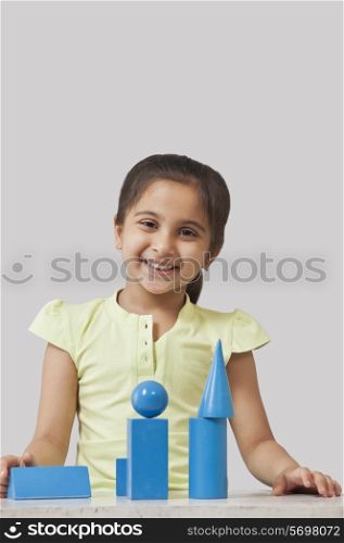 Portrait of little girl with geometry shaped blocks isolated over gray background