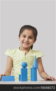 Portrait of little girl with geometry shaped blocks isolated over gray background