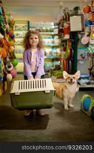 Portrait of little girl with her corgi dog at pet shop. Little child standing with new transportation carrier for puppy. Portrait of little girl with her corgi dog at pet shop