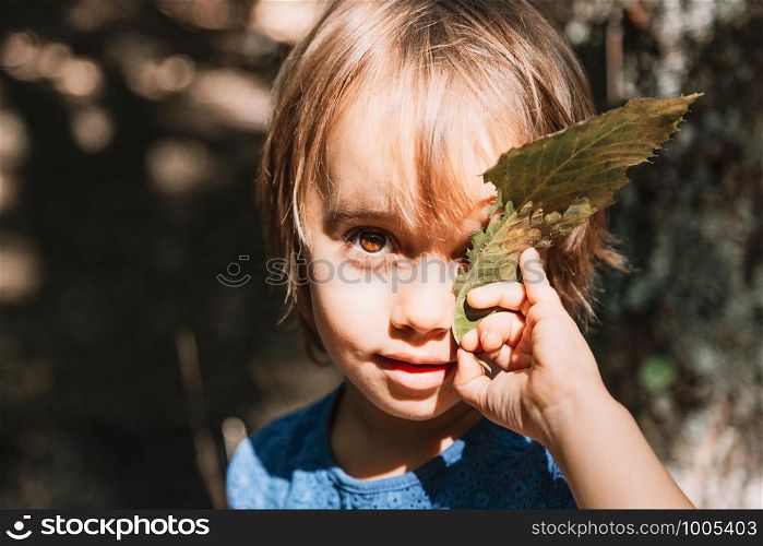Portrait of little girl with leaf in her face in the forest