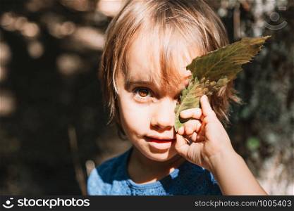 Portrait of little girl with leaf in her face in the forest