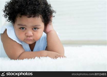 Portrait of little sad African American chubby kid girl is crying with tears rolled down her cheeks while lying on fluffy carpet on floor at home. Child emotion care concept. White background