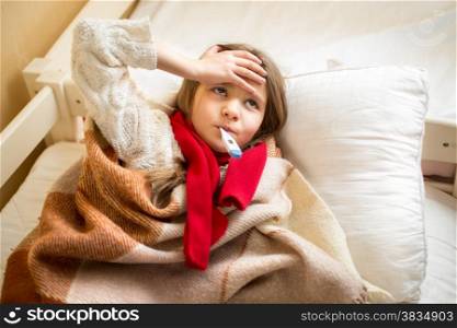 Portrait of little sick girl measuring temperature and holding hand on head