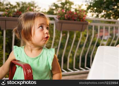 Portrait of little small girl blonde hair eating fruits watermelon in summer day by the table on her balcony