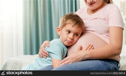 Portrait of little toddler boy hugging and listening to future baby in pregnant mothers belly.. Portrait of little toddler boy hugging and listening to future baby in pregnant mothers belly