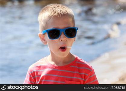Portrait of little young boy kid at sea. Summer.. Portrait of little young boy kid child in sunglasses licking lollipop at sea. Summer holidays vacation.