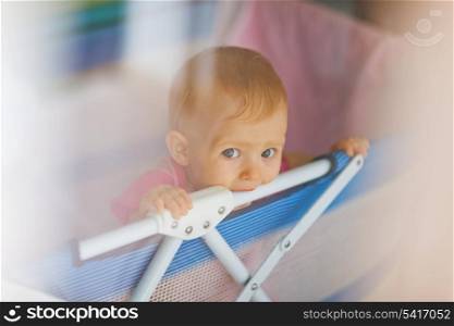 Portrait of lonely baby standing in playpen