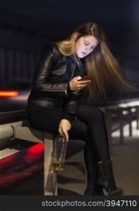 Portrait of lonely woman sitting at highway with whiskey and using mobile phone