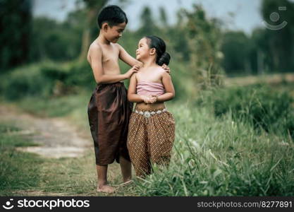 Portrait of Lovely Asian boy shirtless and girl in Thai traditional dress and put beautiful flower on her ear, standing hand in hand and looking on the sky with smiling, copy space