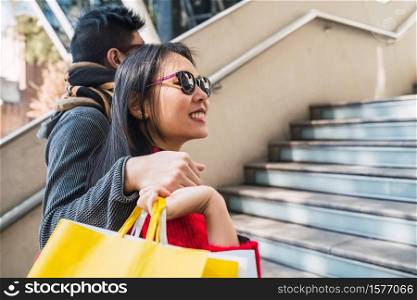 Portrait of lovely Asian couple holding colorful shopping bags and enjoying shopping, having fun together in mall.