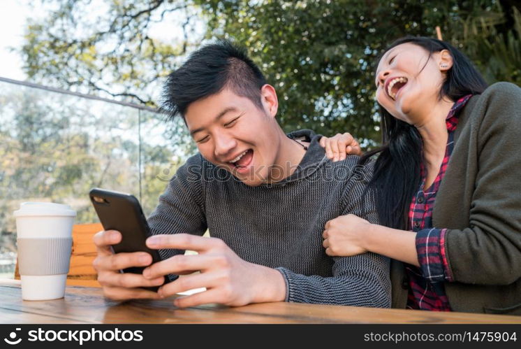 Portrait of lovely asian couple looking at the mobile phone while sitting and spending time at the coffee shop. Love and technology concept.