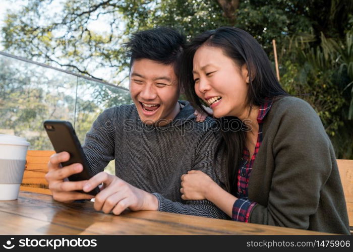 Portrait of lovely asian couple looking at the mobile phone while sitting and spending time at the coffee shop. Love and technology concept.