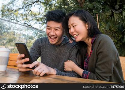 Portrait of lovely asian couple looking at the mobile phone while sitting and spending time at the coffee shop. Love and technology concept.