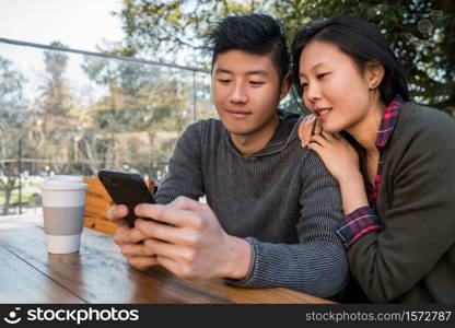 Portrait of lovely asian couple looking at the mobile phone while sitting and spending time at the coffee shop. Love and technology concept.