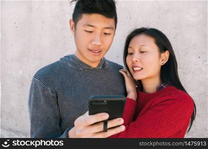 Portrait of lovely asian couple looking at the mobile phone while spending good time together. Love and technology concept.