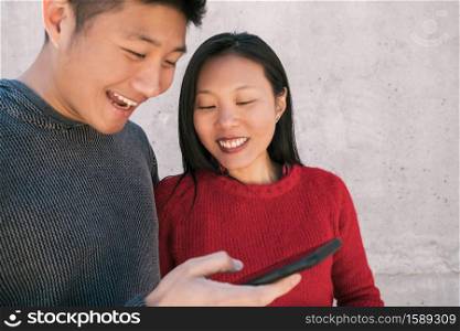 Portrait of lovely asian couple looking at the mobile phone while spending good time together. Love and technology concept.