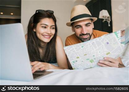 Portrait of lovely couple organizing their trip with a laptop at the hotel room. Travel and holiday concept.