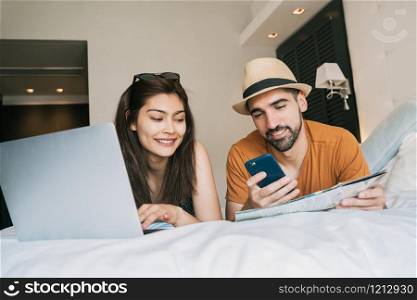 Portrait of lovely couple organizing their trip with laptop and mobile phone at the hotel room. Travel and holiday concept.