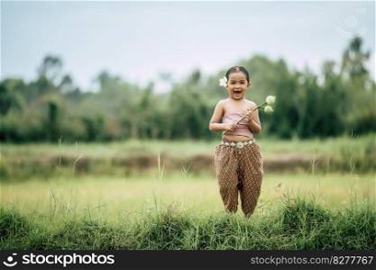 Portrait of lovely girls in Thai traditional dress and put white flower on her ear,  Standing and hold two lotus in hand on rice field, She laughing with happiness and look at camera, copy space