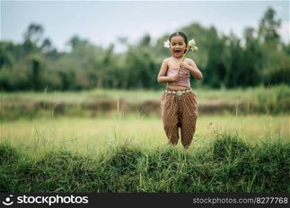 Portrait of lovely girls in Thai traditional dress and put white flower on her ear,  Standing and hold two lotus in hand on rice field, She laughing with happiness and look at camera, copy space