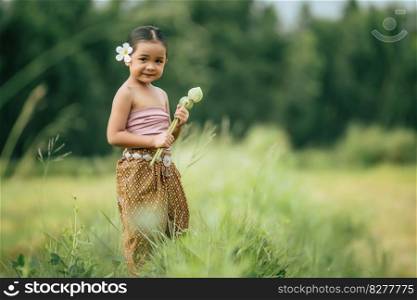 Portrait of lovely girls in Thai traditional dress and put white flower on her ear,  Standing and hold two lotus in hand on rice field, She smile with happiness and looking camera, copy space