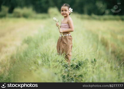 Portrait of lovely girls in Thai traditional dress and put white flower on her ear,  Standing and hold two lotus in hand on rice field, She smile with happiness and looking camera, copy space