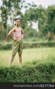Portrait of lovely girls in Thai traditional dress standing posture with arms akimbo on rice field, She smile with happiness and looking camera, copy space