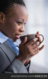 Portrait of lovely happy african business woman with mug in hands relaxing warming and looking at window