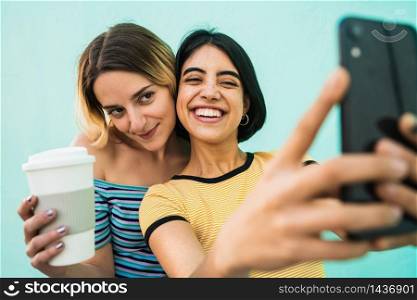 Portrait of lovely lesbian couple having fun and taking a selfie with mobile phone against light blue background. LGBT concept.