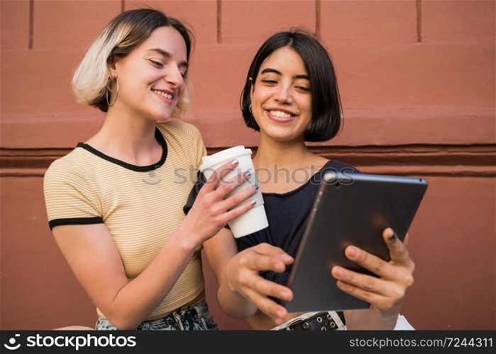 Portrait of lovely lesbian couple spending time together and taking selfie with digital tablet outdoors at the street. LGBT concept.
