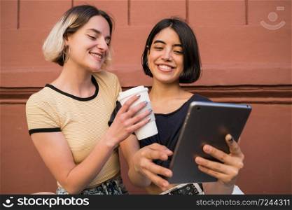 Portrait of lovely lesbian couple spending time together and taking selfie with digital tablet outdoors at the street. LGBT concept.