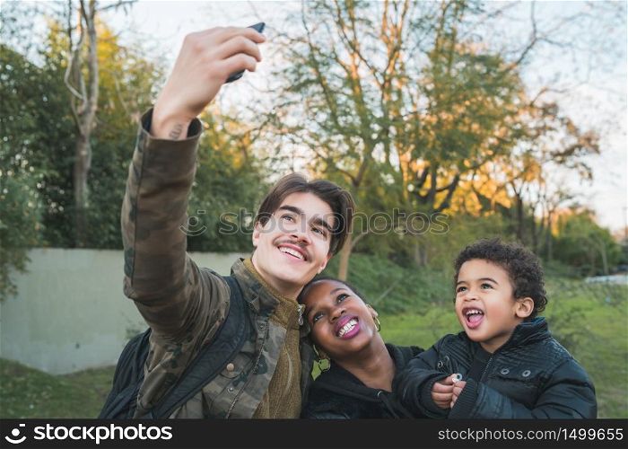 Portrait of lovely mixed race ethnic family having fun and taking a selfie with mobile phone at the park outdoors.