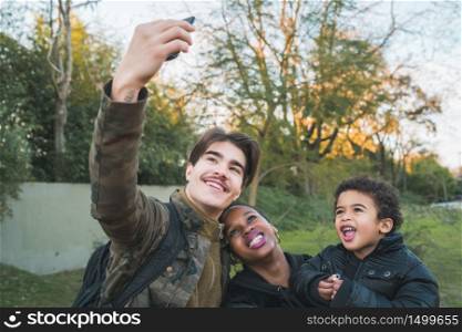 Portrait of lovely mixed race ethnic family having fun and taking a selfie with mobile phone at the park outdoors.