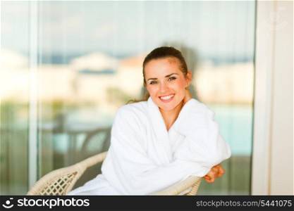 Portrait of lovely smiling woman in bathrobe sitting at terrace&#xA;
