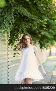 Portrait of lovely urban girl in short white dress in the street. Portrait of a happy smiling woman. Fashionable blonde girl having fun outdoors in the city