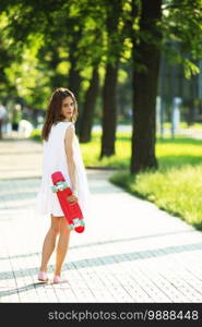 Portrait of lovely urban girl in white dress with a pink skateboard. Happy smiling woman. Girl holding a plastic skate board outdoors. City life.