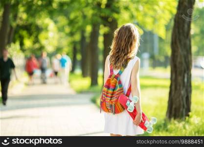 Portrait of lovely urban girl in white dress with a pink skateboard. Happy smiling woman. Girl holding a plastic skate board outdoors. City life. Back view