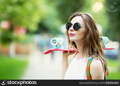 Portrait of lovely urban girl in white dress with a pink skateboard. Happy smiling woman. Girl holding a plastic skate board outdoors. City life.