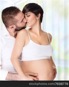 Portrait of loving couple at home, handsome man with tenderness kissing with his beautiful pregnant wife, enjoying pregnancy, happy family life 