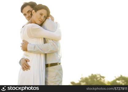 Portrait of loving man embracing woman in park against clear sky